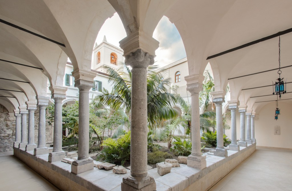 Historic cloister courtyard at San Domenico Palace, a Four Seasons hotel in Taormina, Sicily, blending monastic architecture with lush Mediterranean gardens.