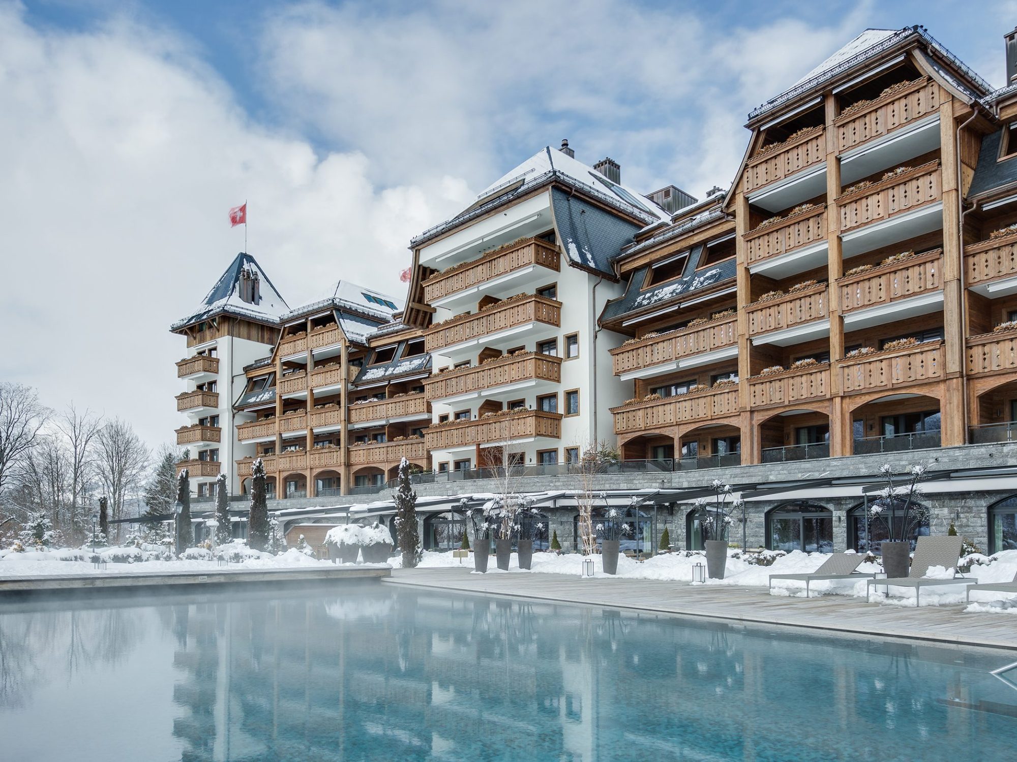 The Alpina Gstaad luxury five-star hotel in the Swiss Alps, featuring its outdoor infinity pool with panoramic mountain views and elegant chalet-style architecture.