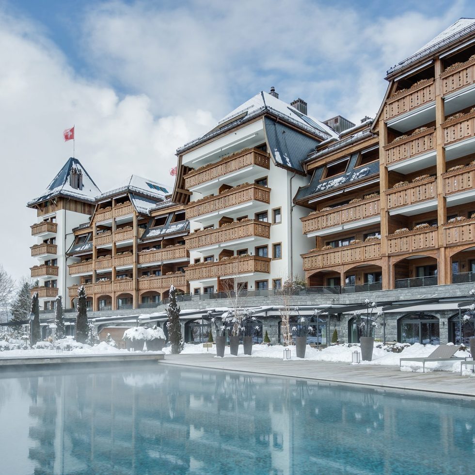 The Alpina Gstaad luxury five-star hotel in the Swiss Alps, featuring its outdoor infinity pool with panoramic mountain views and elegant chalet-style architecture.