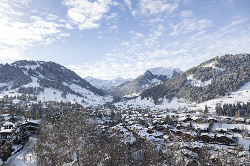 Panoramic view of Gstaad village and the surrounding Swiss Alps from The Alpina Gstaad luxury hotel, showcasing the charming alpine landscape.