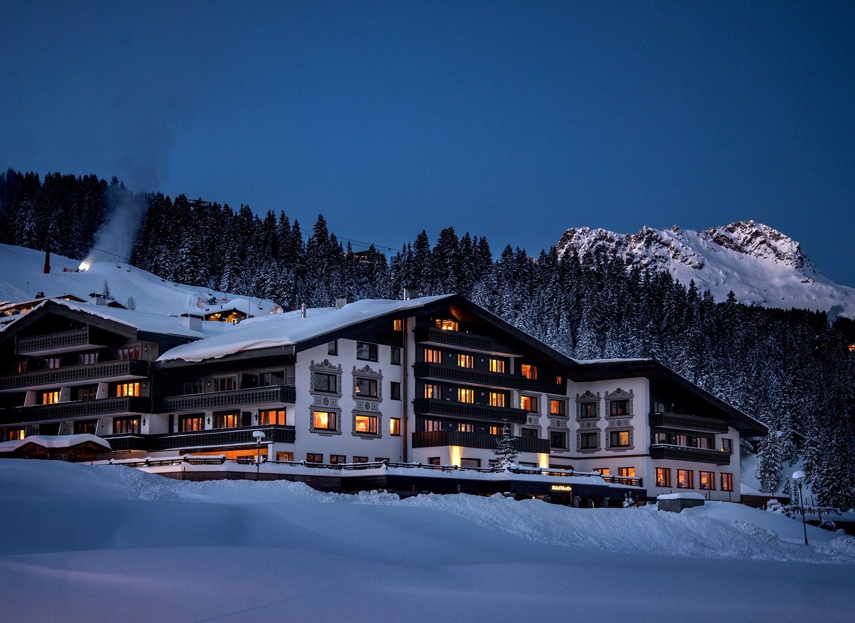 Exterior view of the Almhof Schneider in Lech am Arlberg, showcasing its traditional alpine architecture set against a snowy mountain landscape.