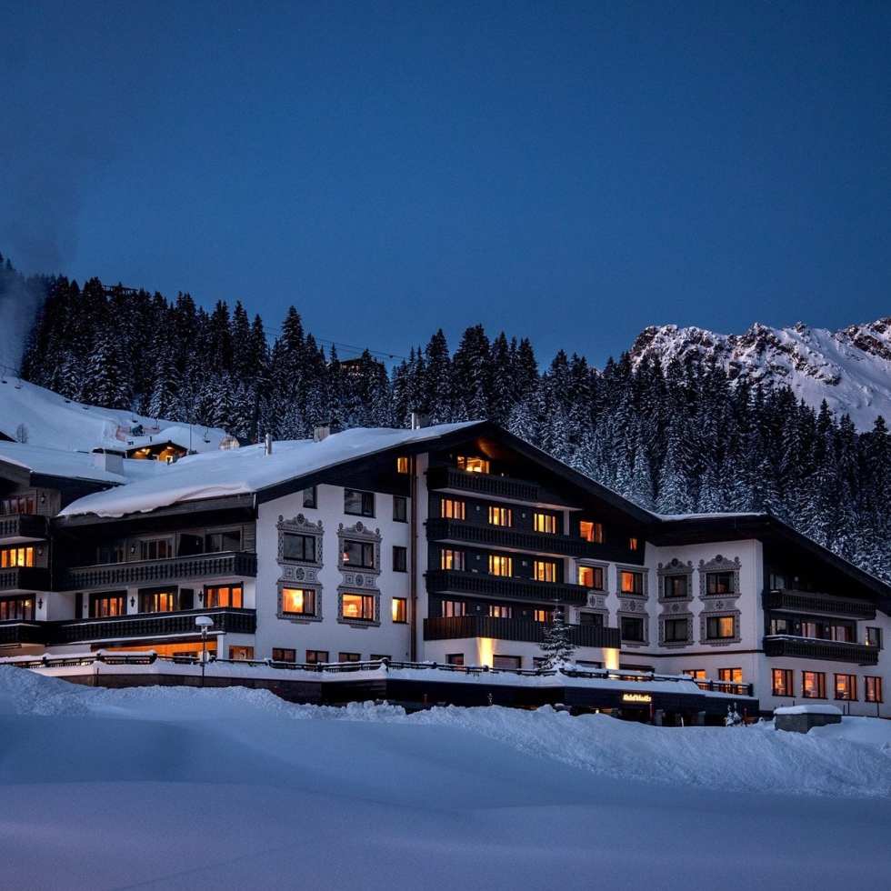 Exterior view of the Almhof Schneider in Lech am Arlberg, showcasing its traditional alpine architecture set against a snowy mountain landscape.