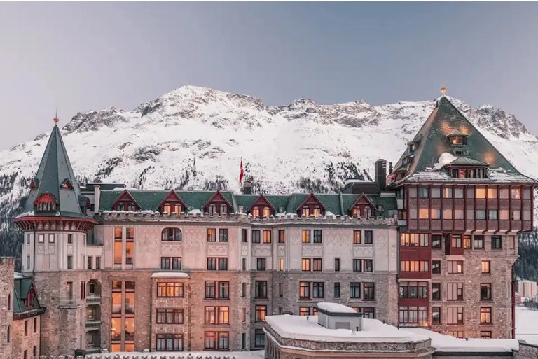 Exterior view of Badrutt’s Palace Hotel overlooking Lake St. Moritz, with its historic tower rising above the Engadin landscape.