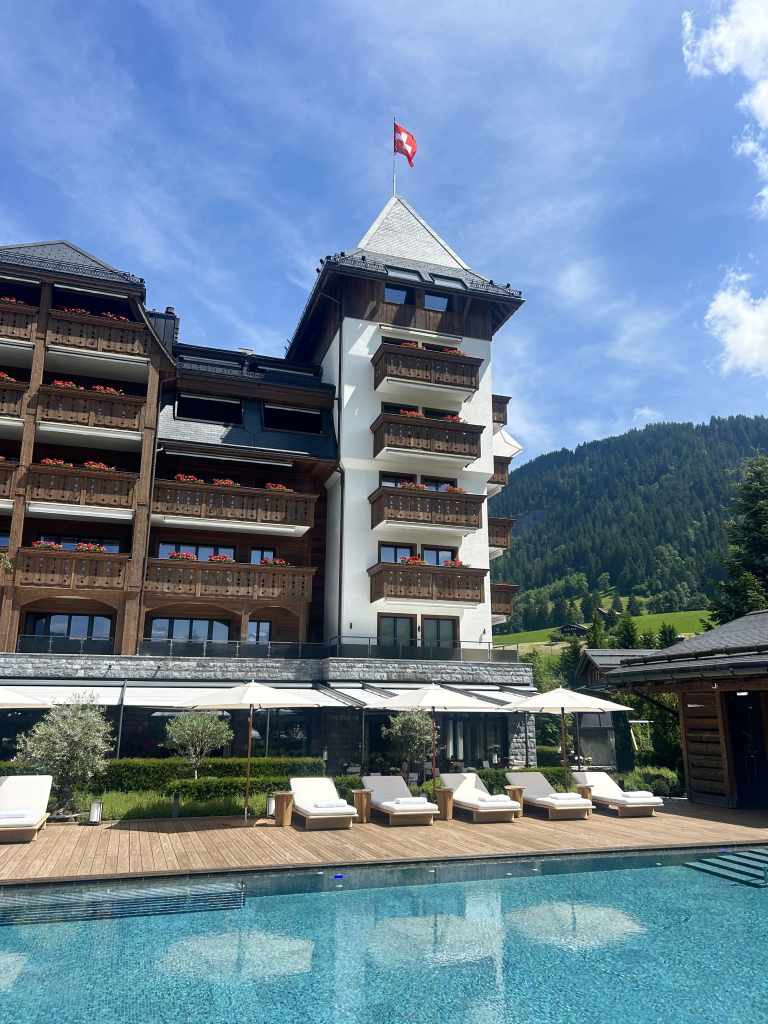 Outdoor pool and sunbeds at The Alpina Gstaad with the iconic tower in the background on a sunny summer day