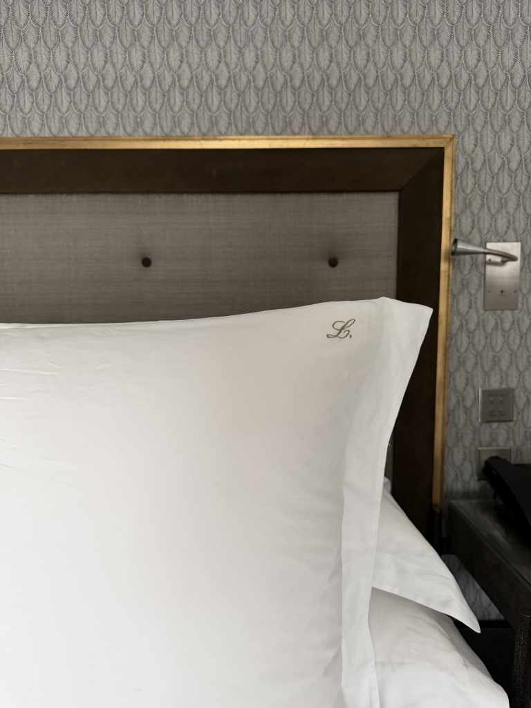 Close-up of a pillow case featuring embroidered guest initials, placed on a neatly made bed inside a luxury hotel suite, highlighting personalized in-room details.